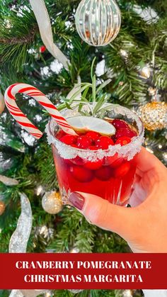 a hand holding a drink in front of a christmas tree with the words cranberry pomegranate christmas margarita