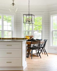 An amber vase and orange flowers sit on a circular table. The kitchen table decor is surrounded by black chairs. A square light frame hangs above the table in front of the shiplap walling...   Image: athomeontheboulevard