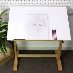 a desk with a drawing on it next to a potted plant and two pencils