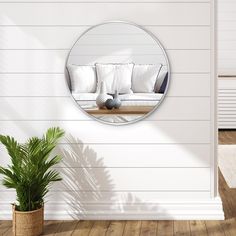 a living room with white walls and wood flooring has a round mirror on the wall