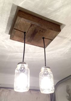 two mason jars are hanging from the ceiling in front of a mirror and light fixture