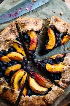 a pie with sliced peaches and blueberries on a cutting board next to a knife