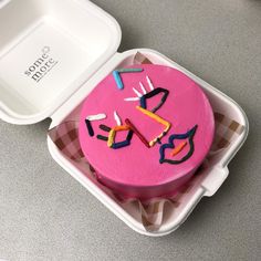 a pink cake sitting in a white container on top of a gray table next to a fork and knife