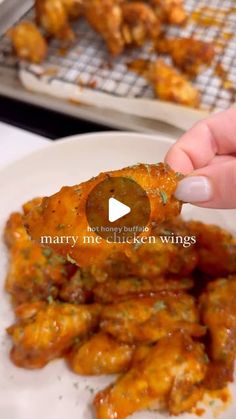 a person is picking up some chicken wings from a white plate on a table with other food items in the background