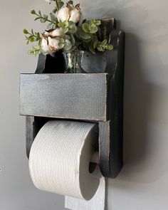 a toilet paper dispenser with some flowers in it on the wall next to a roll of toilet paper