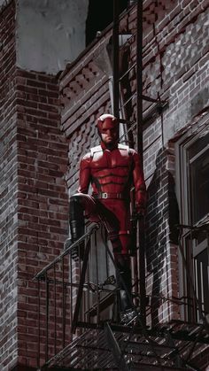 a man in a red suit standing on top of a set of stairs next to a brick building