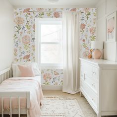 a white bed sitting next to a window in a room with pink flowers on the walls