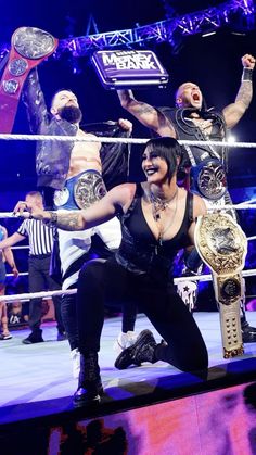 two women and one man are holding up their arms in the air as they stand on top of a wrestling ring