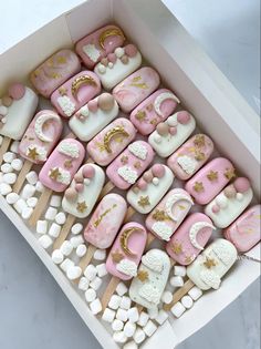 a box filled with pink and gold decorated cookies on top of wooden skewers