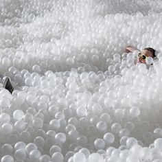 a man in sunglasses is surrounded by white balls that are floating on the ground,