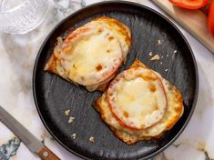 two pieces of bread topped with cheese and sauce on top of a black plate next to sliced tomatoes