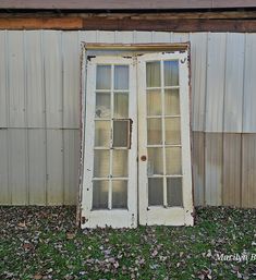 an old double door sitting in the grass next to a building with a metal roof