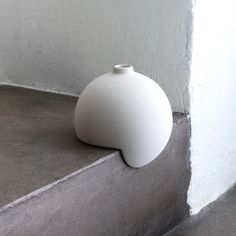 a white vase sitting on the ground next to a wall