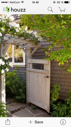 a wooden door is open in front of a house with white flowers on the bushes