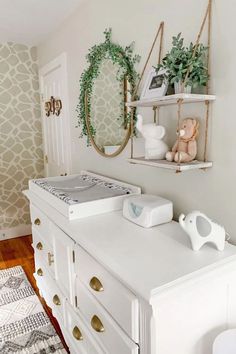 a baby's room with white dressers and wallpaper on the walls, two mirrors above them