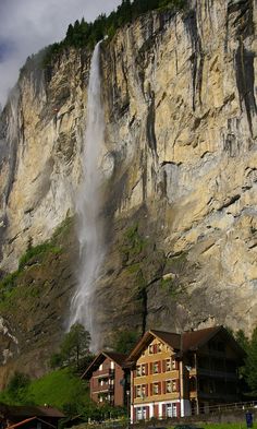 a large waterfall is coming out of the side of a mountain into a town below