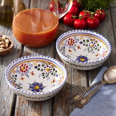 two bowls with spoons on a wooden table next to tomatoes and other food items