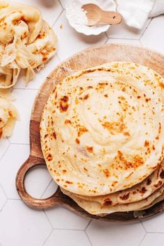 three flatbreads on a wooden plate with some other food items around the bowl