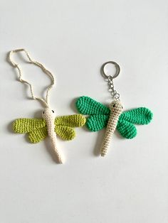 two crocheted dragon keychains on a white surface, one is green and the other is yellow