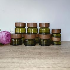 several jars with lids are sitting next to a pink rose on a wooden countertop