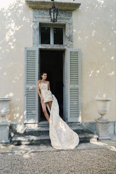 a woman in a white dress is standing on the steps outside an old building with shutters