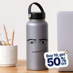 a silver water bottle with a face drawn on it next to a laptop and pencils