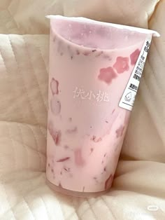 a pink cup with some writing on it sitting on a white bed sheet in front of a pillow