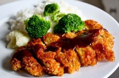 a white plate topped with meat and veggies covered in ketchup next to rice