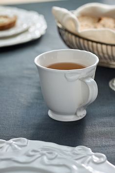 a cup of tea sits on a table with other plates and bowls in the background