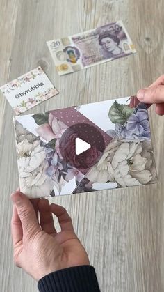 someone is holding an envelope with flowers on it and some money in front of them