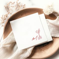 a white card with red ink sitting on top of a wooden plate next to dried flowers