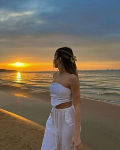 a woman standing on top of a beach next to the ocean at sunset or dawn