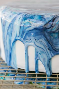 a blue and white cake sitting on top of a cooling rack with icing dripping from it