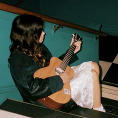 a woman sitting on the ground playing an acoustic guitar