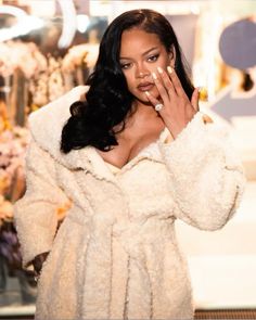 a woman in a fur coat holding her hand up to her face and looking at the camera