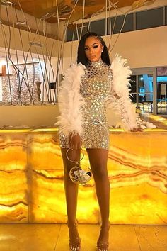 a woman standing in front of a counter wearing a silver dress and white feathered jacket