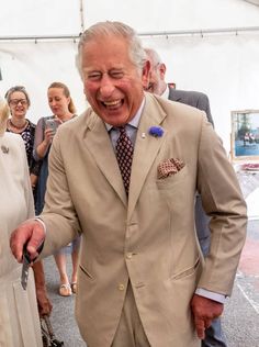 an older man in a tan suit and tie smiles as he walks down the street