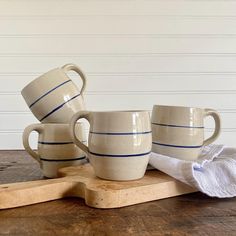 three coffee mugs sitting on top of a wooden table next to a towel and napkin