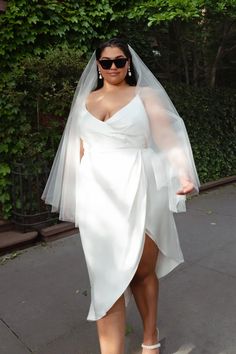 a woman wearing sunglasses and a white dress is walking down the street with her veil over her head