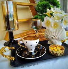 a table topped with a cup of coffee next to a vase filled with white flowers