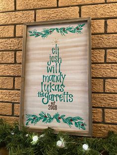 a wooden sign hanging from the side of a brick wall next to a christmas tree