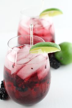 two glasses filled with blackberry limeade on top of a white table next to blackberries