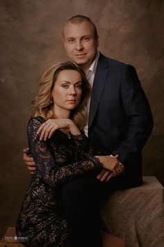 a man and woman are posing for a photo in front of a brown background with their arms around each other