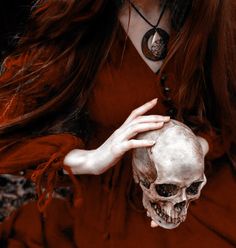 a woman with long red hair holding a skull in her hands and wearing a necklace