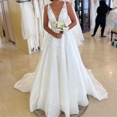 a woman is standing in front of her wedding dress at the bridal shop wearing a white gown