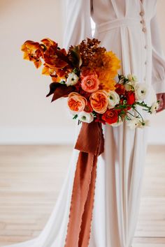 a woman holding a bouquet of flowers in her hand and wearing a long white dress