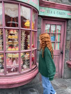 a woman with red hair standing in front of a pink store window and looking at cakes