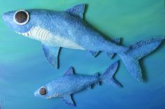 two blue plastic sharks are in the water with their mouths open and one is bigger than the other