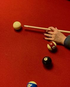 a woman's hand reaching for pool balls on a red table with cues