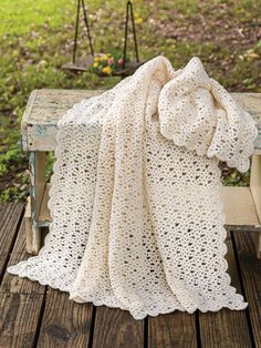 a white crocheted blanket sitting on top of a wooden bench